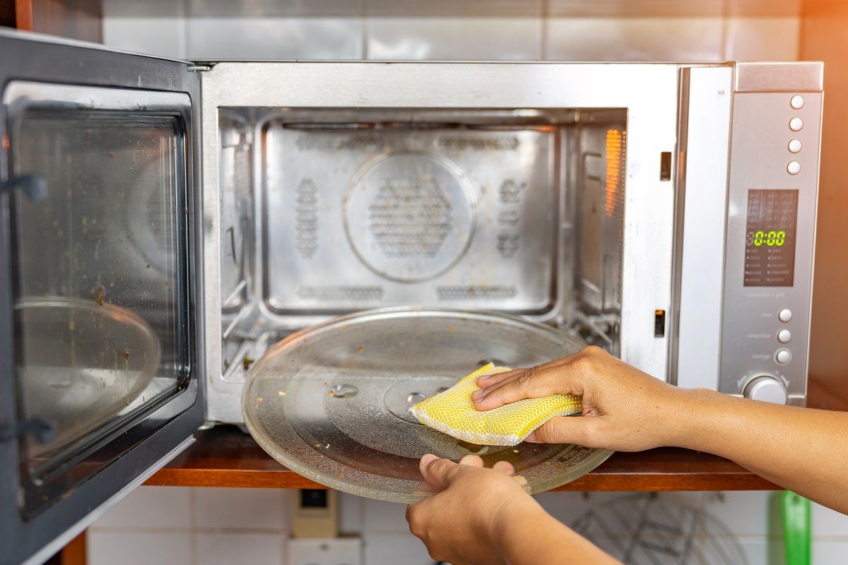 Woman,Cleaning,Turn,Disk,In,Microwave,Oven,With,Sponge.