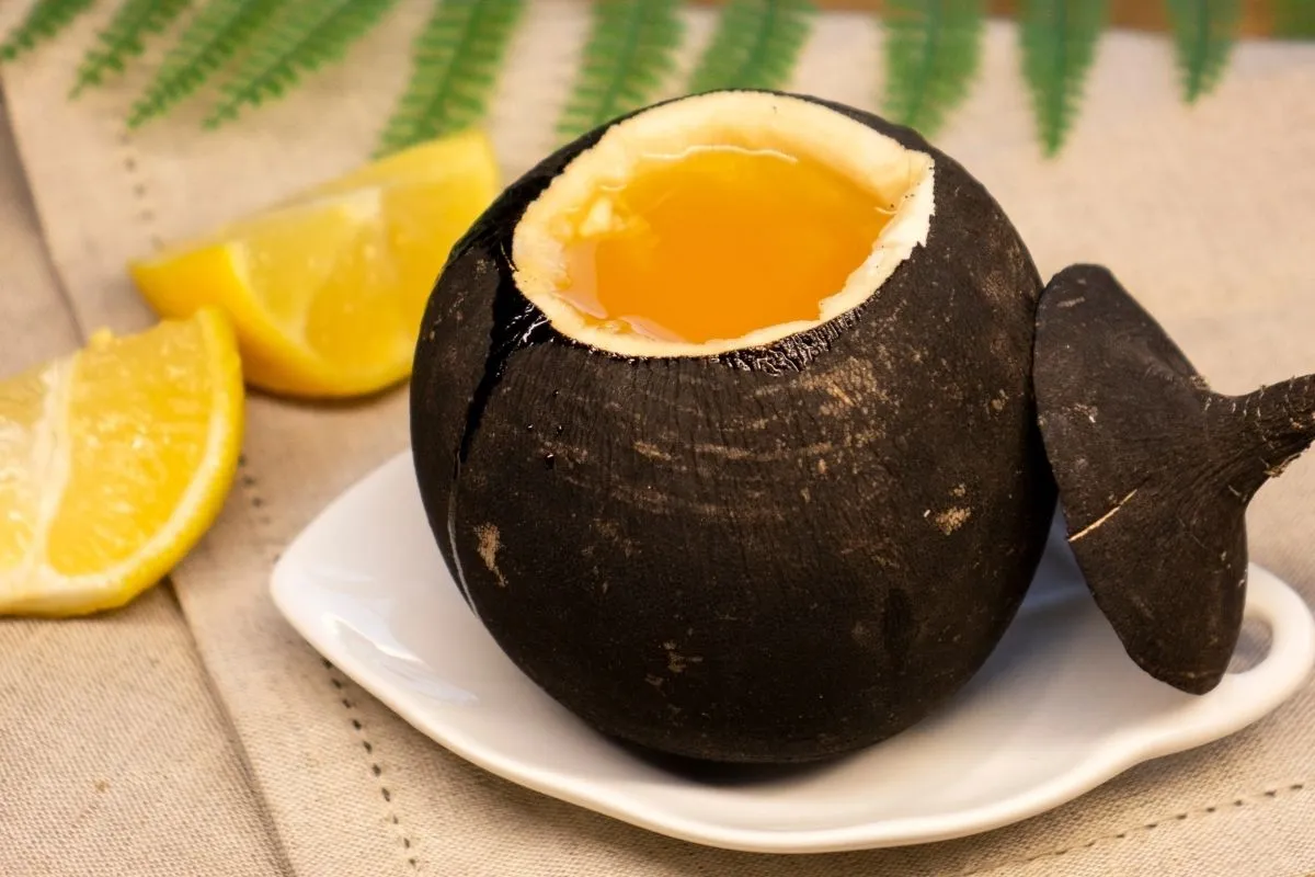 Fekete retek szirup egy fehér tányéron, citromok a háttérben