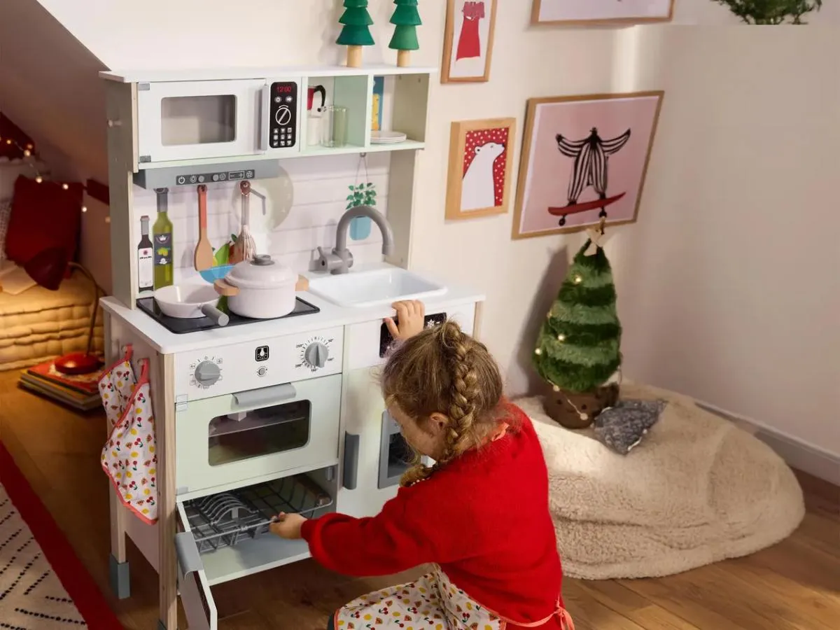 Kislány játszik a Lidl fa játékkonyhájával ünnepi környezetben