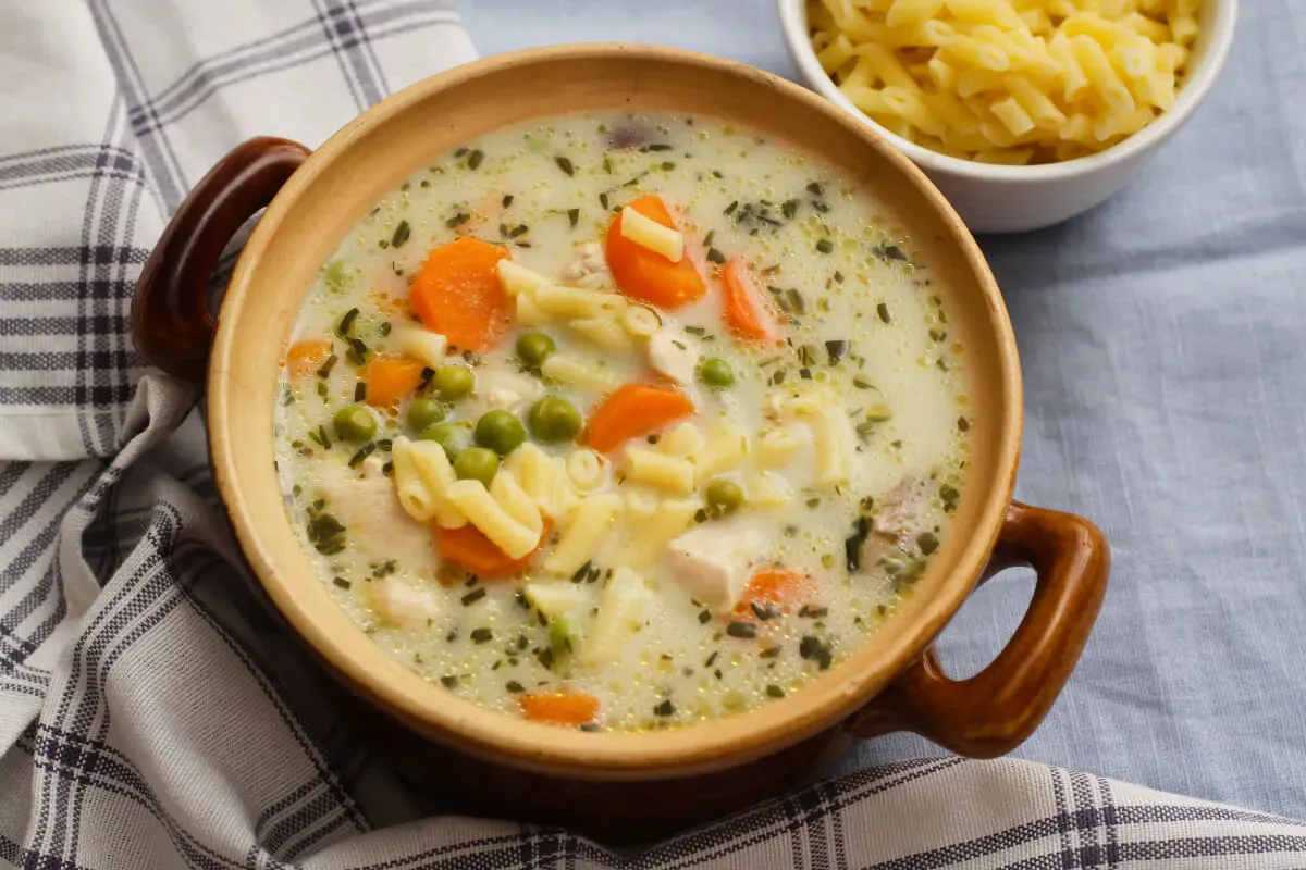 Egy tál gőzölgő tárkonyos csirkeraguleves kockás konyharuhán