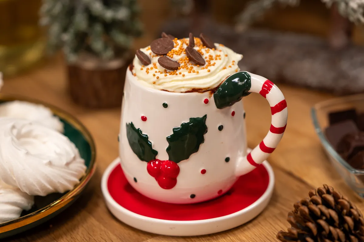 Forró csokoládé: egy szép karácsonyi bögrében, karácsonyi díszek között tejszínhabos forró csoki