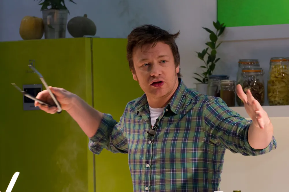 Jamie Oliver kockás ingben áll a konyhában egy csipesszel a kezében