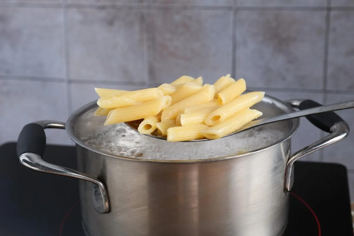 Tésztafőzés: egy lábosban lobogó vízből kanállal pennét vesz ki valaki