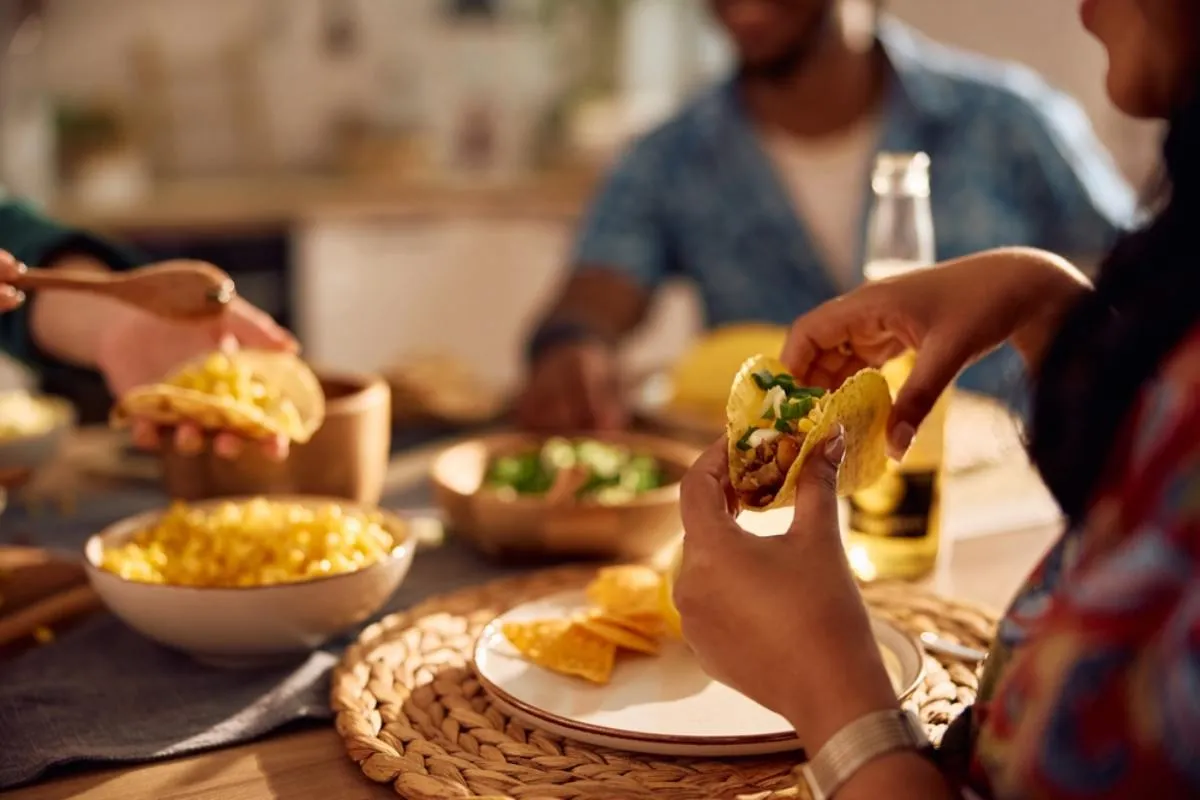 Hétvégi ebéd: egy asztalnál többen ülnek, egy nő éppen tacót eszik