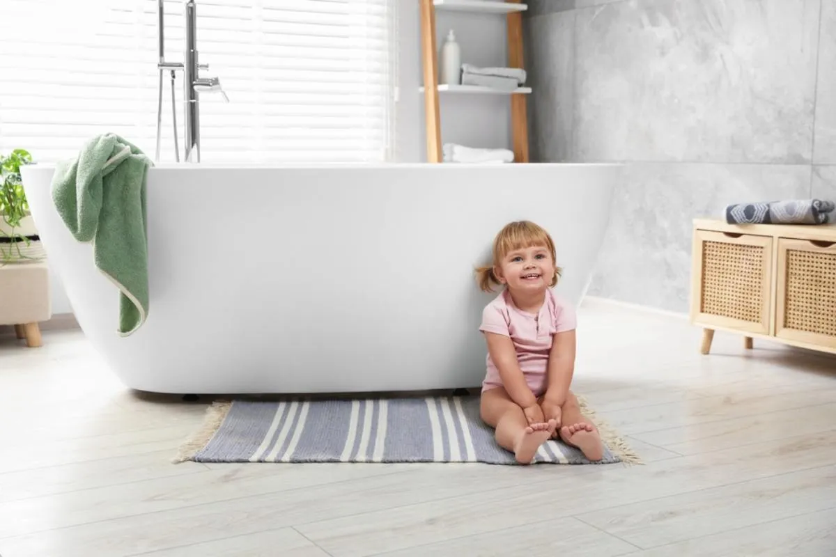 Fürdőszobai szőnyegek: egy kislány ül a fürdőkád előtt a szőnyegen