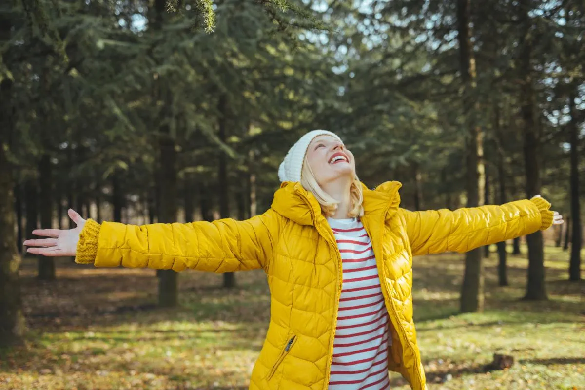 A japán légzéses séta segít a pozitív változásokat: egy nő sárga kabátban áll az erdőben