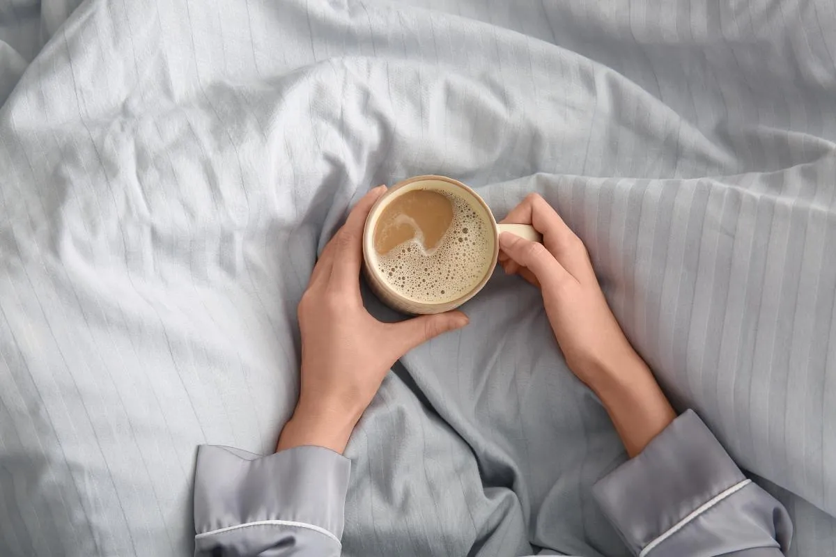 Kávé éhgyomorra? Ágyban ülő nő kezében egy csésze kávé