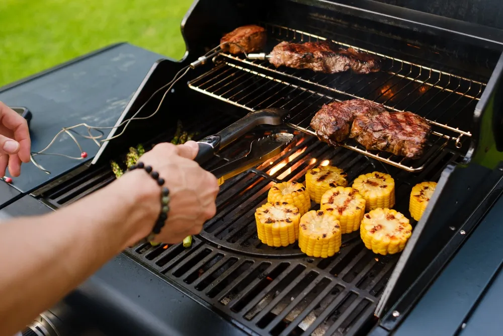 A,Person,Is,Grilling,Steaks,And,Corn,On,A,Barbecue.