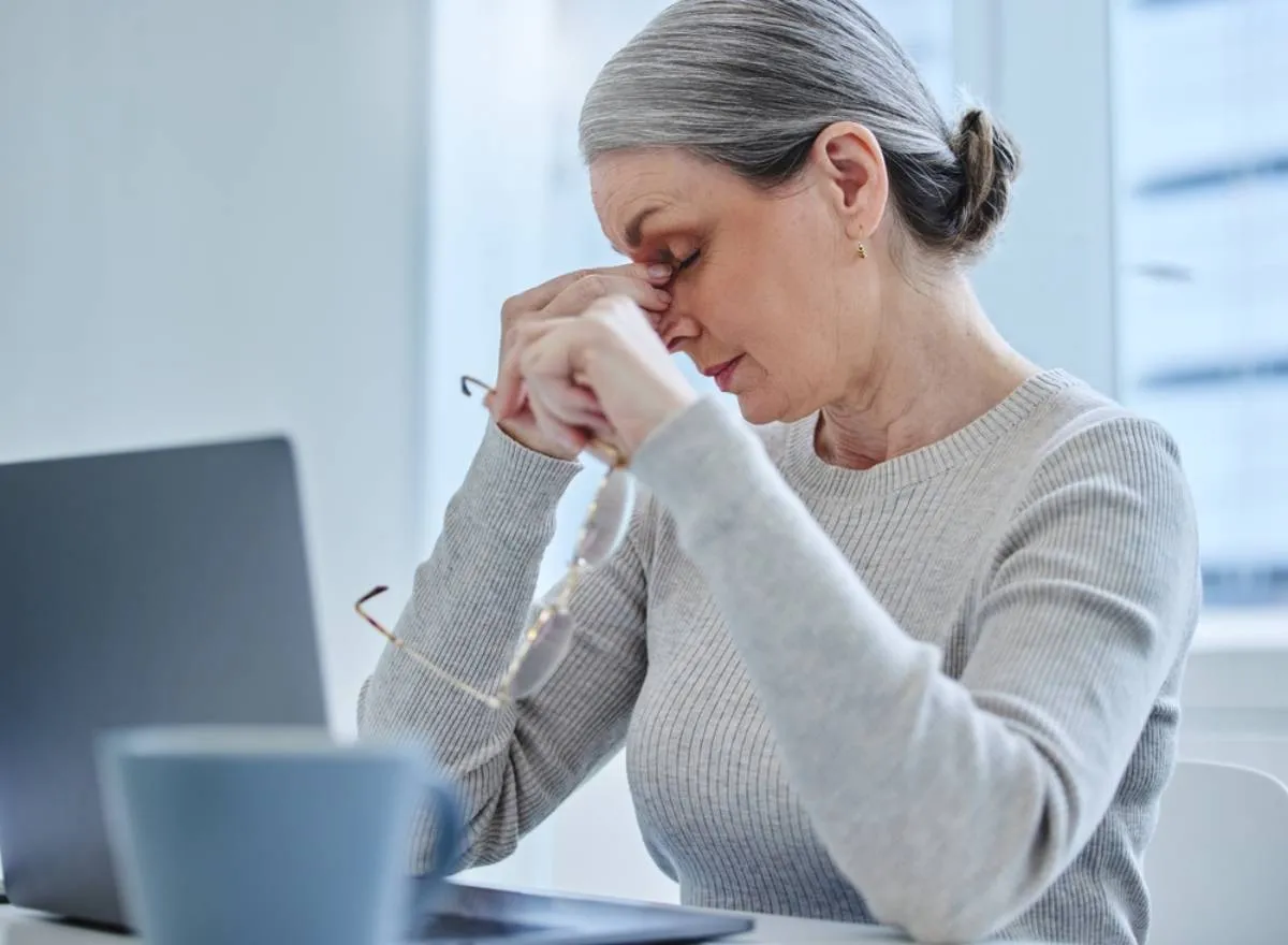 Menopauza: változókorban lévő nő ül a számítógép előtt és masszírozza a fejét
